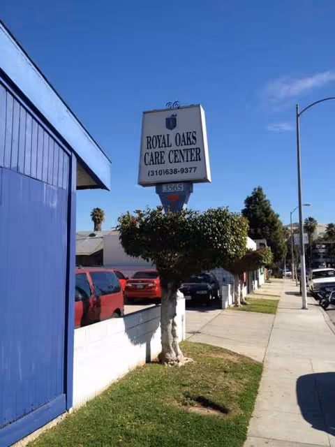 A sidewalk view of Royal Oaks Care Center exterior with a sign and blue building.