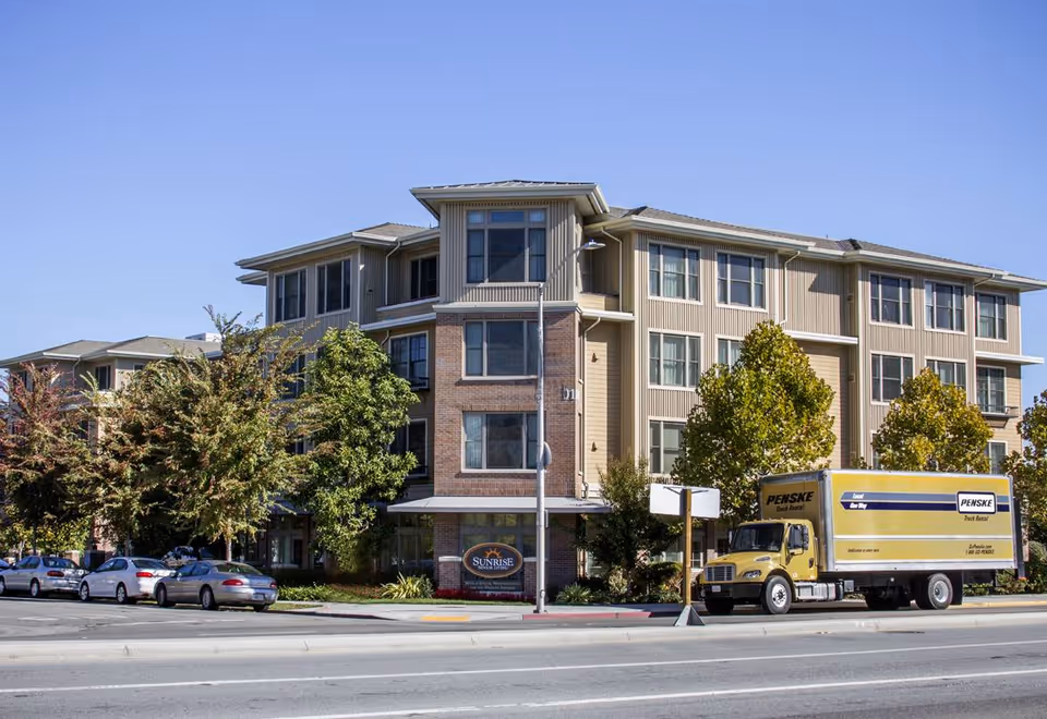 Exterior view of a multi-story senior living building with a Penske truck parked on the street in front.