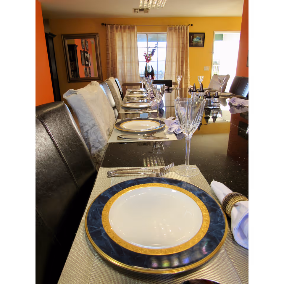 Long dining table set with plates, wine glasses and napkins in a brightly colored dining room.