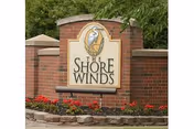 Brick entrance sign reading The Shore Winds with flowers and greenery.