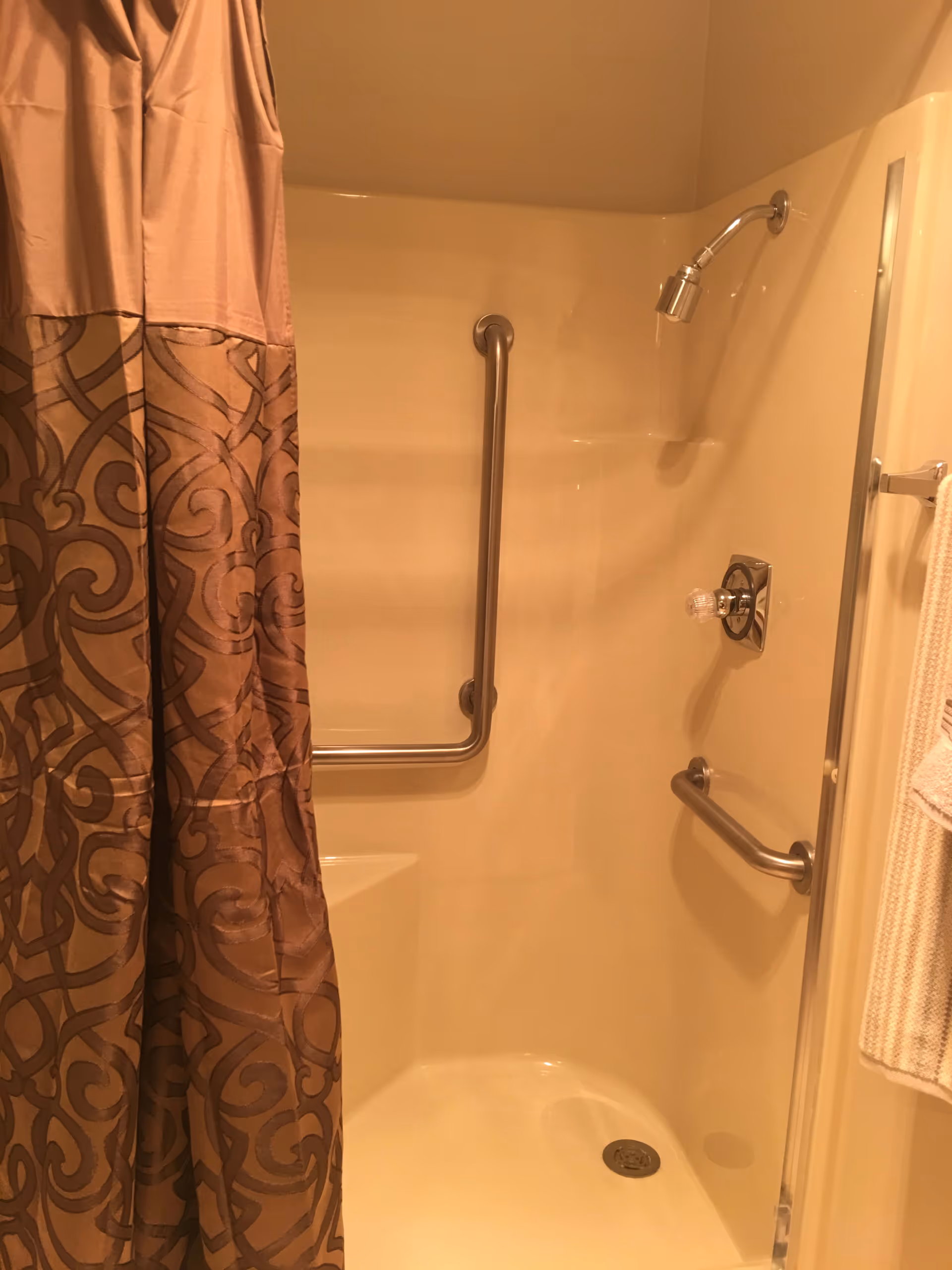 Shower stall with a decorative curtain, grab bars, showerhead and towel on a rack.
