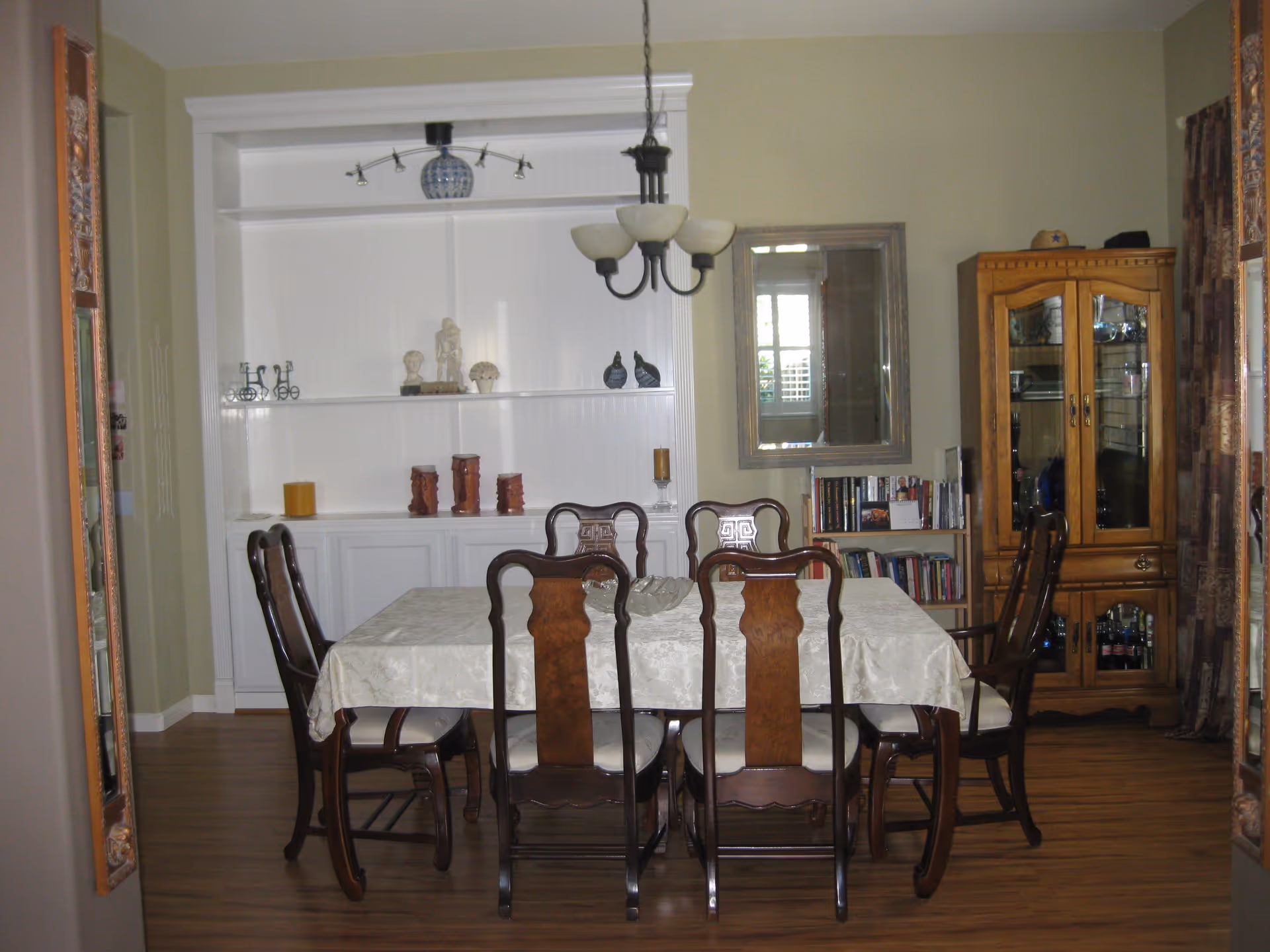 Dining room with a table covered by a tablecloth surrounded by wooden chairs, a chandelier, built-in shelving, and a china cabinet.