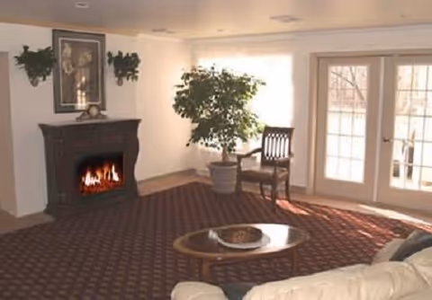 Cozy living room with a fireplace, potted plant, coffee table, sofa, and French doors letting in natural light.