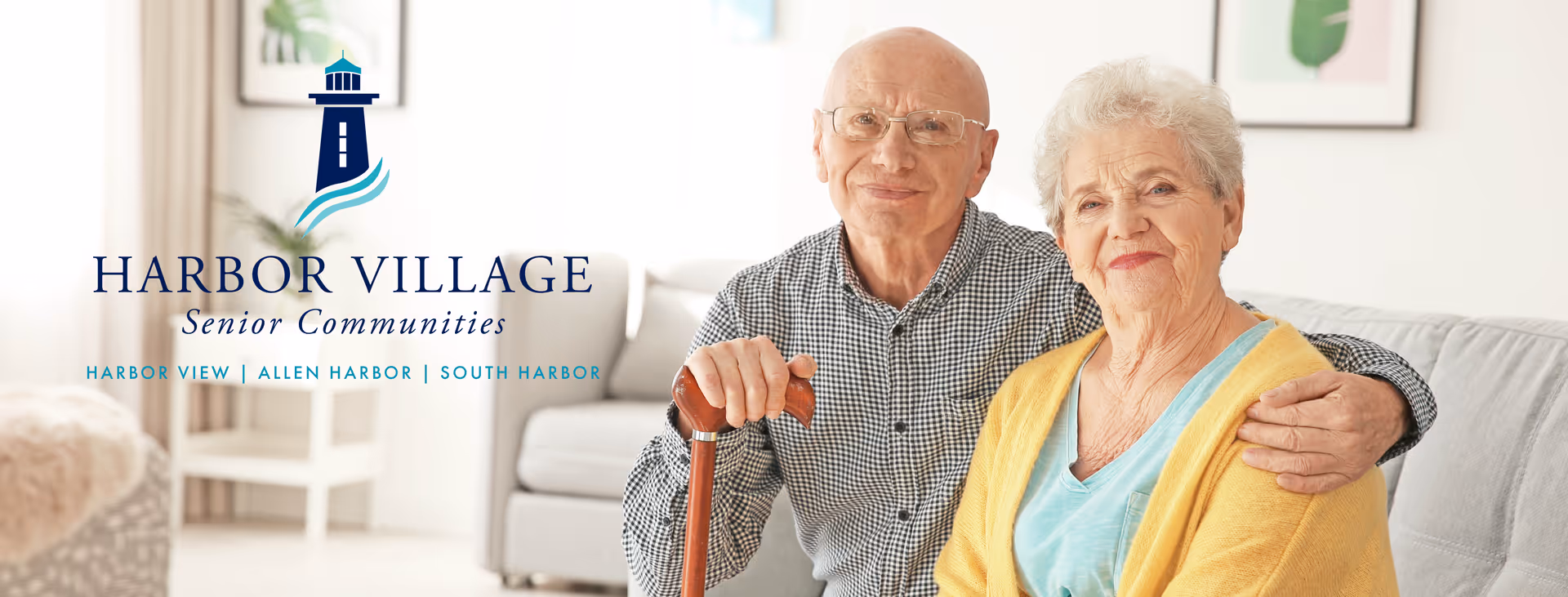 An elderly man and woman seated on a living room sofa with the Harbor Village Senior Communities logo on the left.