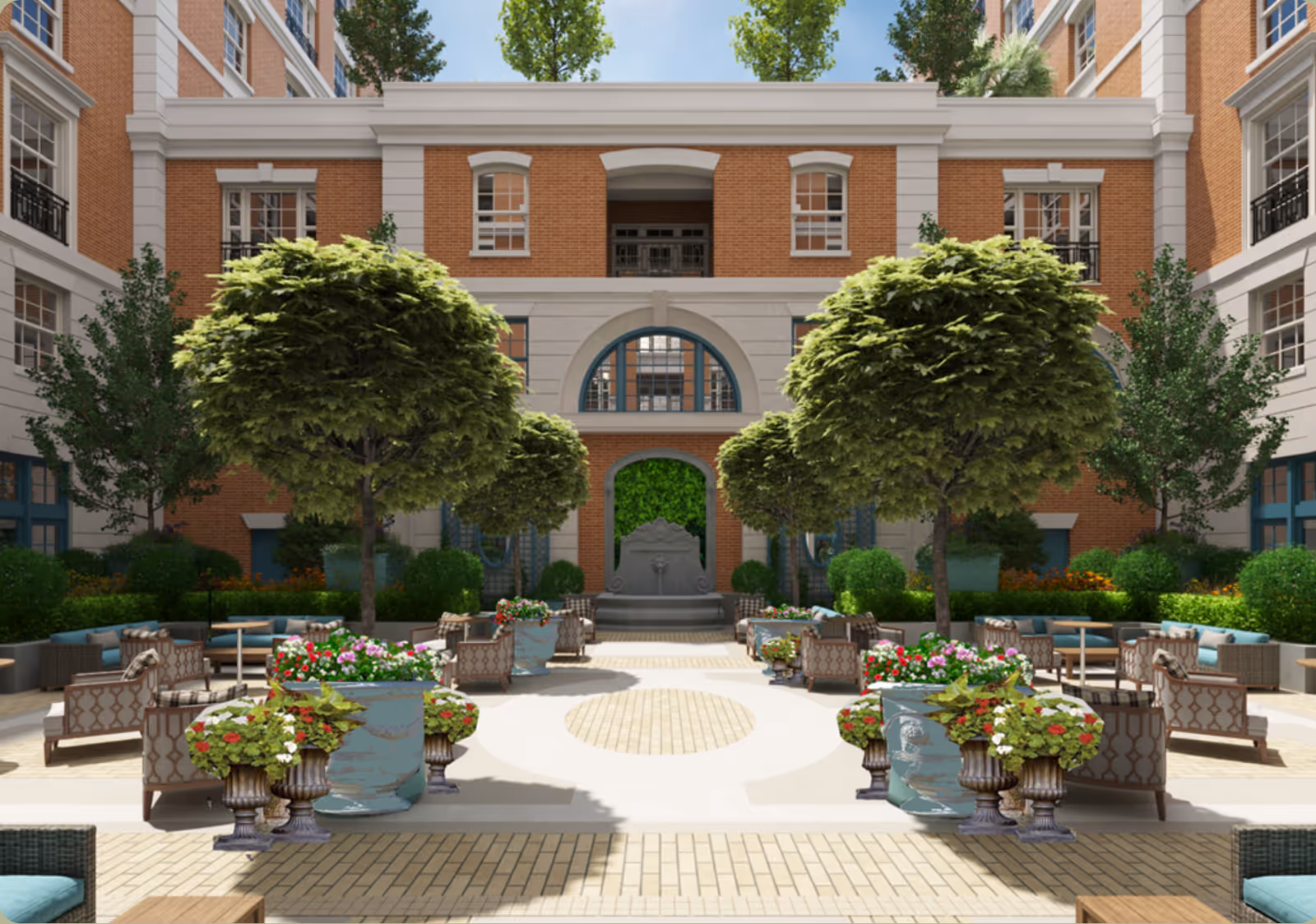 Outdoor courtyard area at The Peninsula of Charleston featuring neatly arranged seating with cushioned chairs and sofas, large potted plants with colorful flowers, several trimmed trees, and a decorative stone fountain against a brick and stone building backdrop.