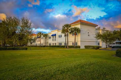 Exterior view of Banyan Place senior living facility with a green lawn and palm trees.