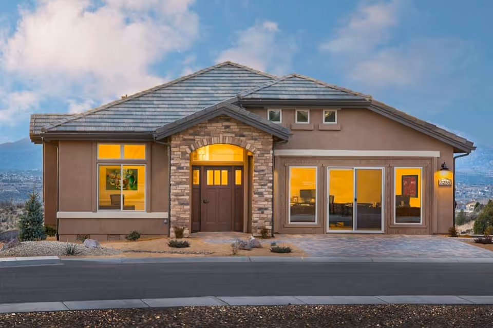 Front exterior view of a single-story house with a stone archway entrance, large windows, and a tiled roof under a partly cloudy sky.