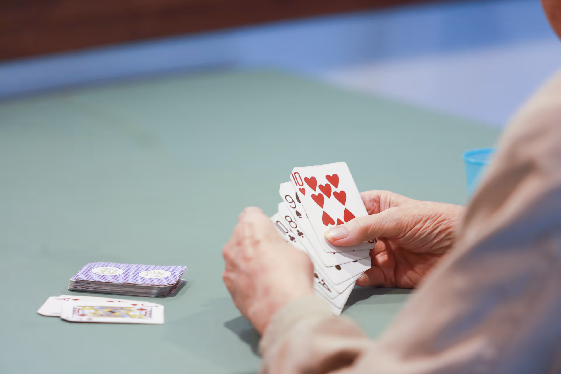 Close-up of an elderly person holding playing cards at a table with a deck of cards and some cards laid out on the table.