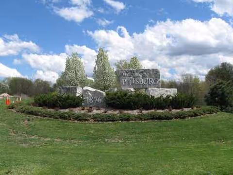 Well-manicured entrance with a stone sign reading 'Welcome to Pittsburg' at Medicalodges Pittsburg.