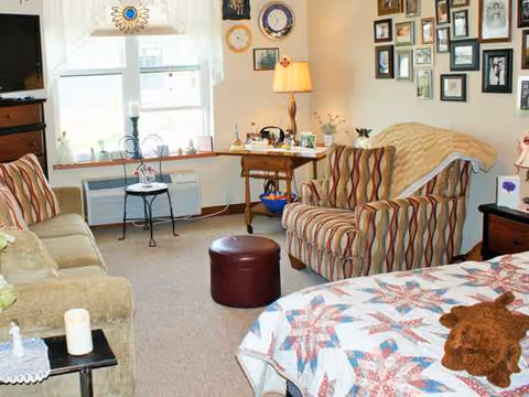 Cozy living room with striped chairs, sofa, quilted bed, and wall photo gallery.