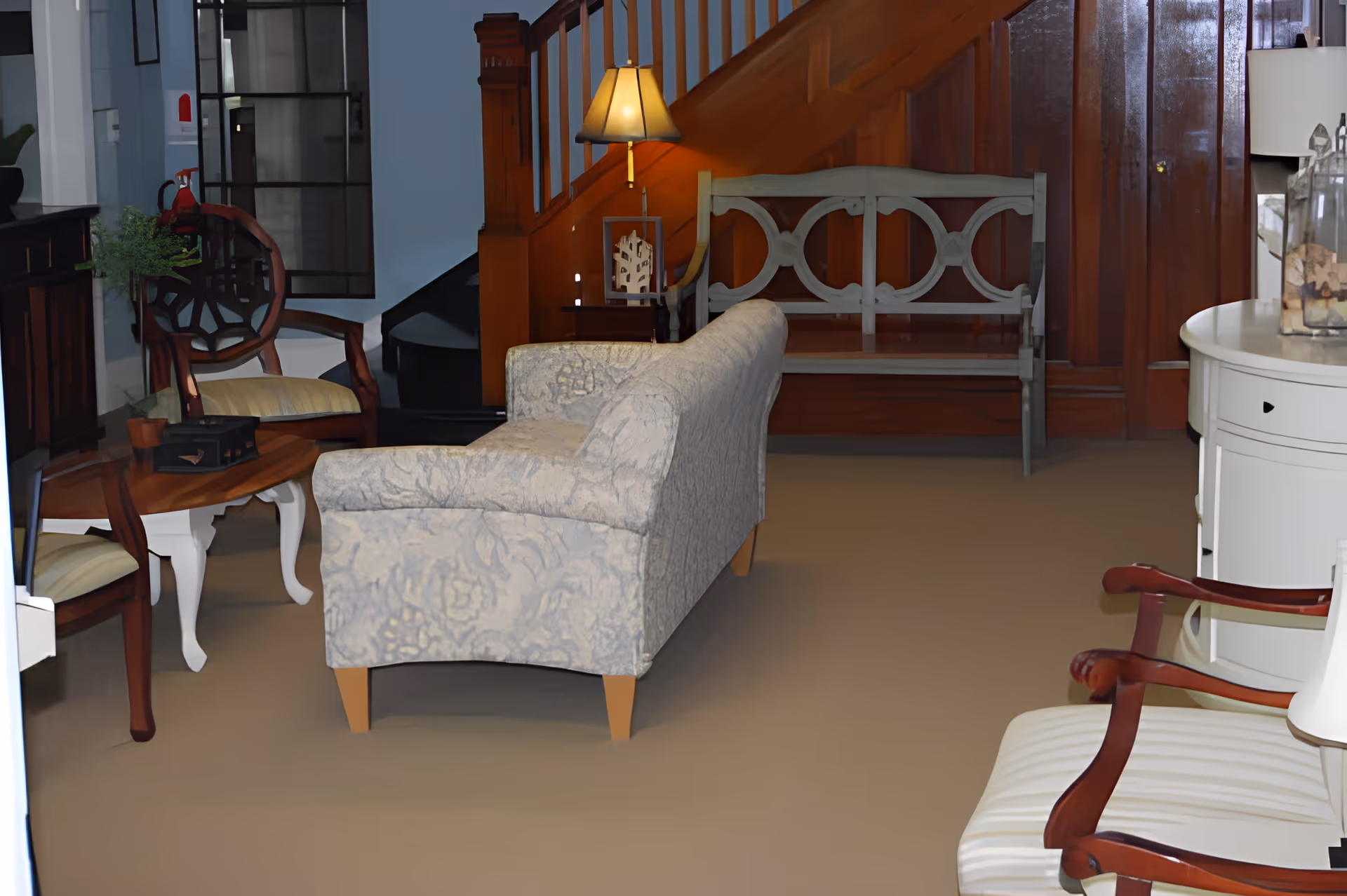 Cozy sitting area with a patterned sofa, wooden chairs, a coffee table and a bench by a wooden staircase.