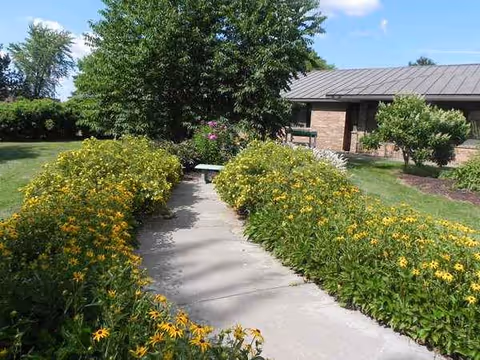 Sunny outdoor garden path lined with yellow flowers leads to Vernon Manor entrance.