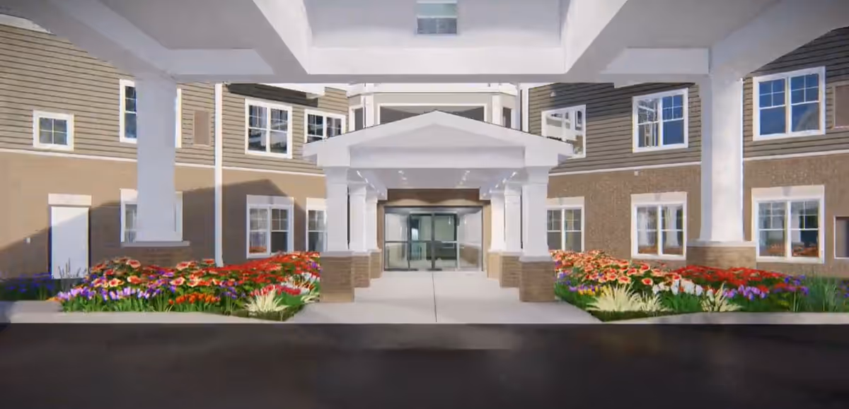 Covered entrance/porte-cochere of a multi-story building with glass doors and colorful flowerbeds.