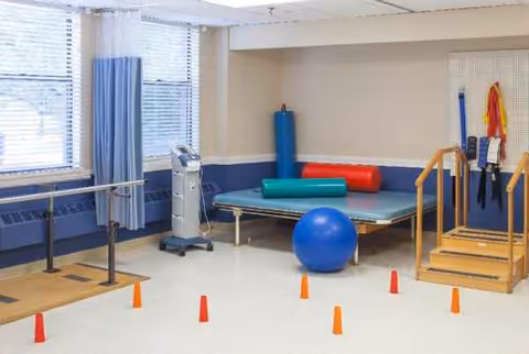 Maplewood Rehabilitation gym with parallel bars, mats, balls, cones, and therapy equipment.