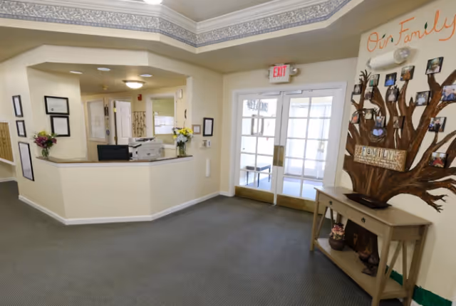 Reception desk and entryway of a senior living facility lobby with a decorative family tree display on a console table.