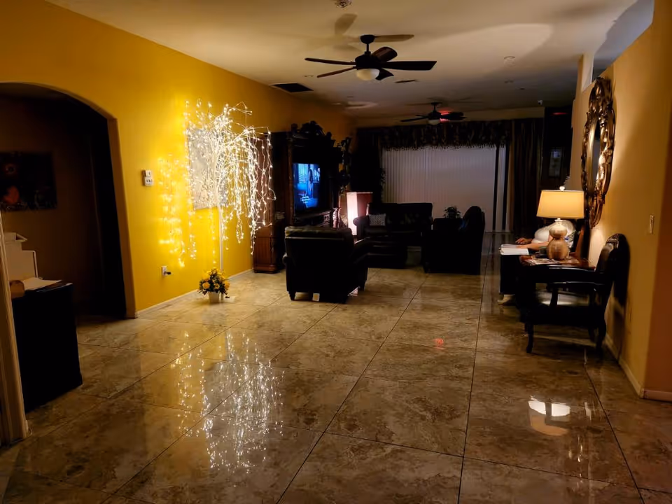 Spacious interior living room with glossy tiled floor, a seating area facing a TV, and an illuminated decorative string-light tree against a yellow wall.