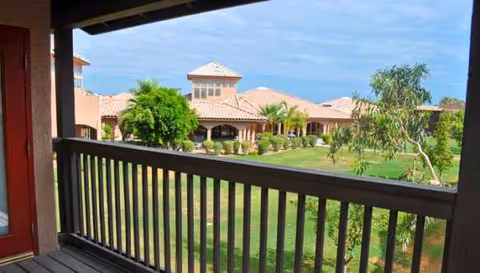 From a balcony, a courtyard with tan stucco buildings and green landscaping.