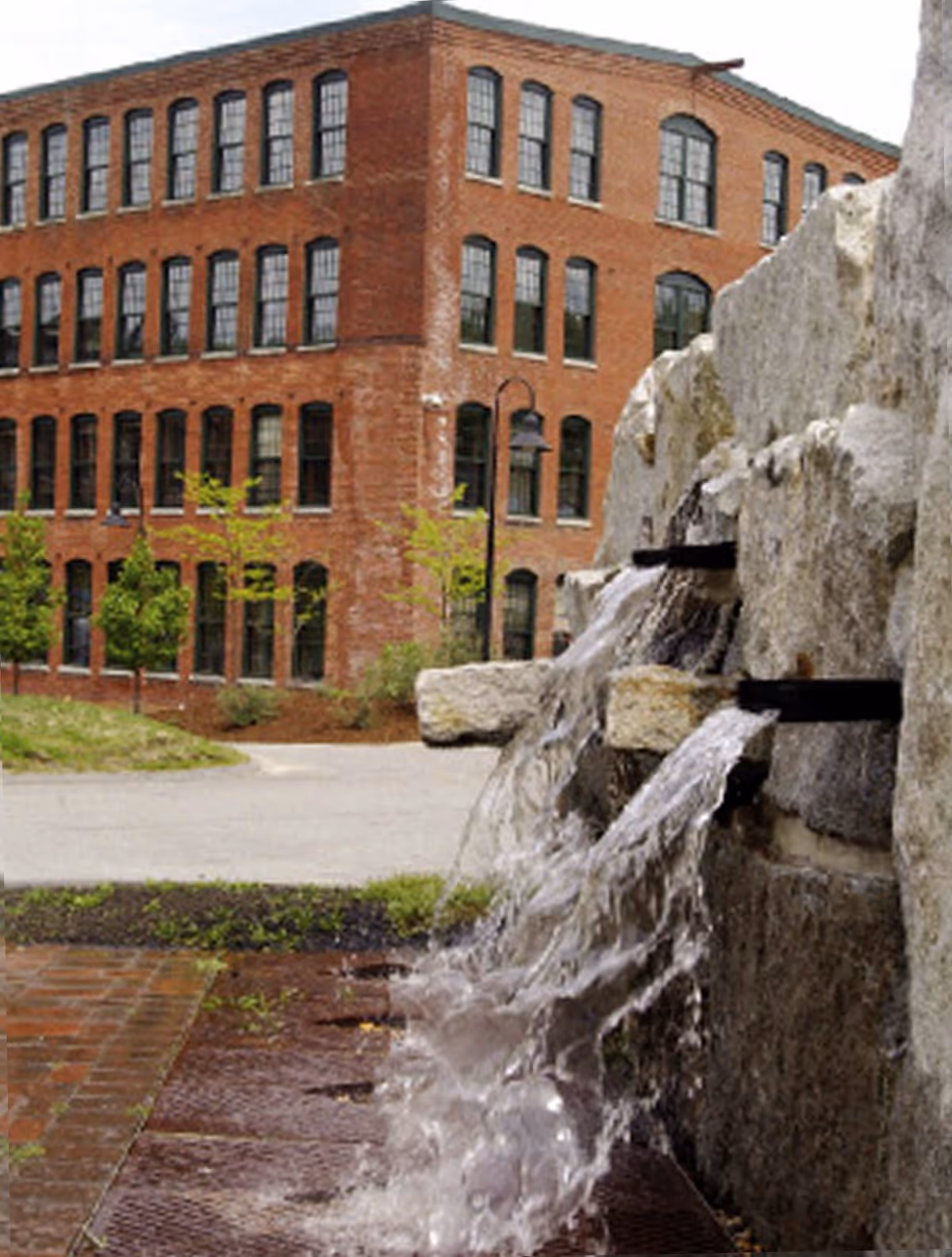 Stone fountain with cascading water in front of a multi-story red brick apartment building.