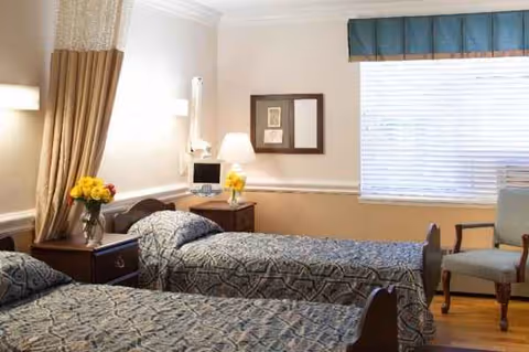 A hotel-style bedroom with two beds, nightstands, lamps, and a window.