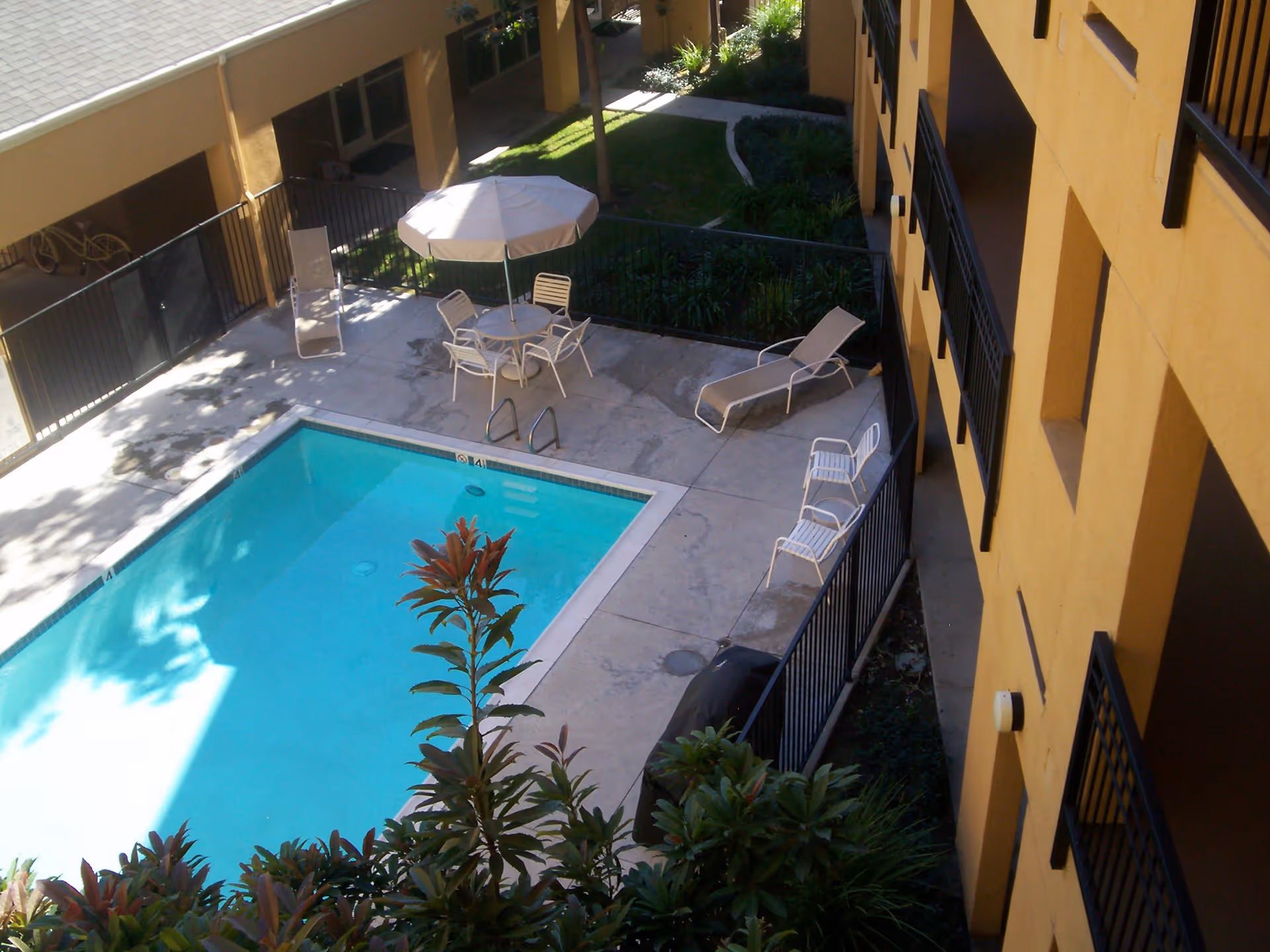 Courtyard swimming pool with lounge chairs, a table and umbrella, and surrounding apartment balconies.