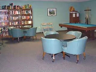 A recreation lounge with a pool table, round table, and blue chairs.