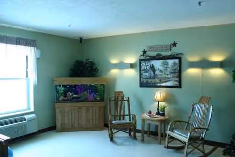 A cozy resident lounge with wicker chairs, a fish tank, framed art, and soft lighting.