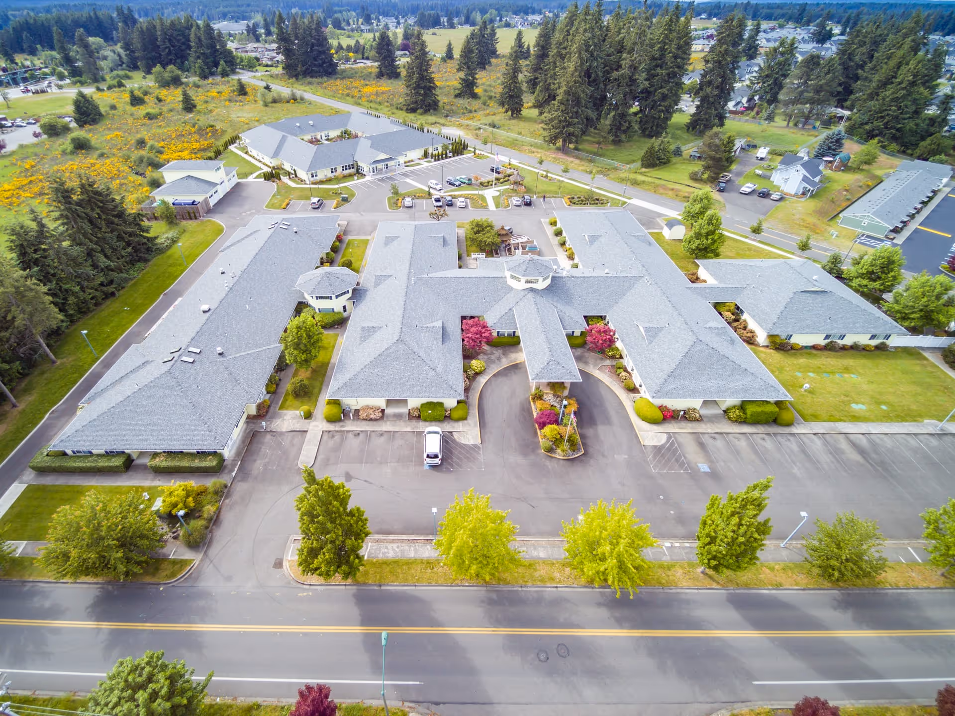 Aerial view of Easthaven Villa Assisted Living & Memory Care facility showing multiple connected buildings with gray roofs, surrounded by trees, parking lots, and green landscaped areas.