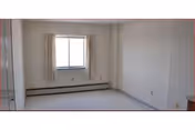 Empty room with a window framed by beige curtains, baseboard heater, light-colored walls, and a closet door.