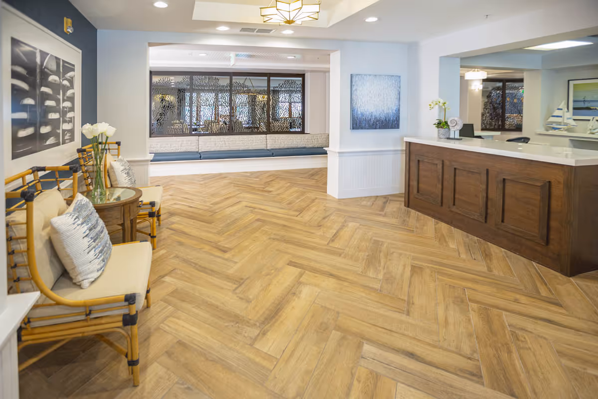 Lobby reception area with a wooden front desk, cushioned seating, decorative wall art, and herringbone wood flooring.