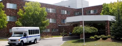 Brick St. Camillus senior living facility exterior with a small bus parked in front.