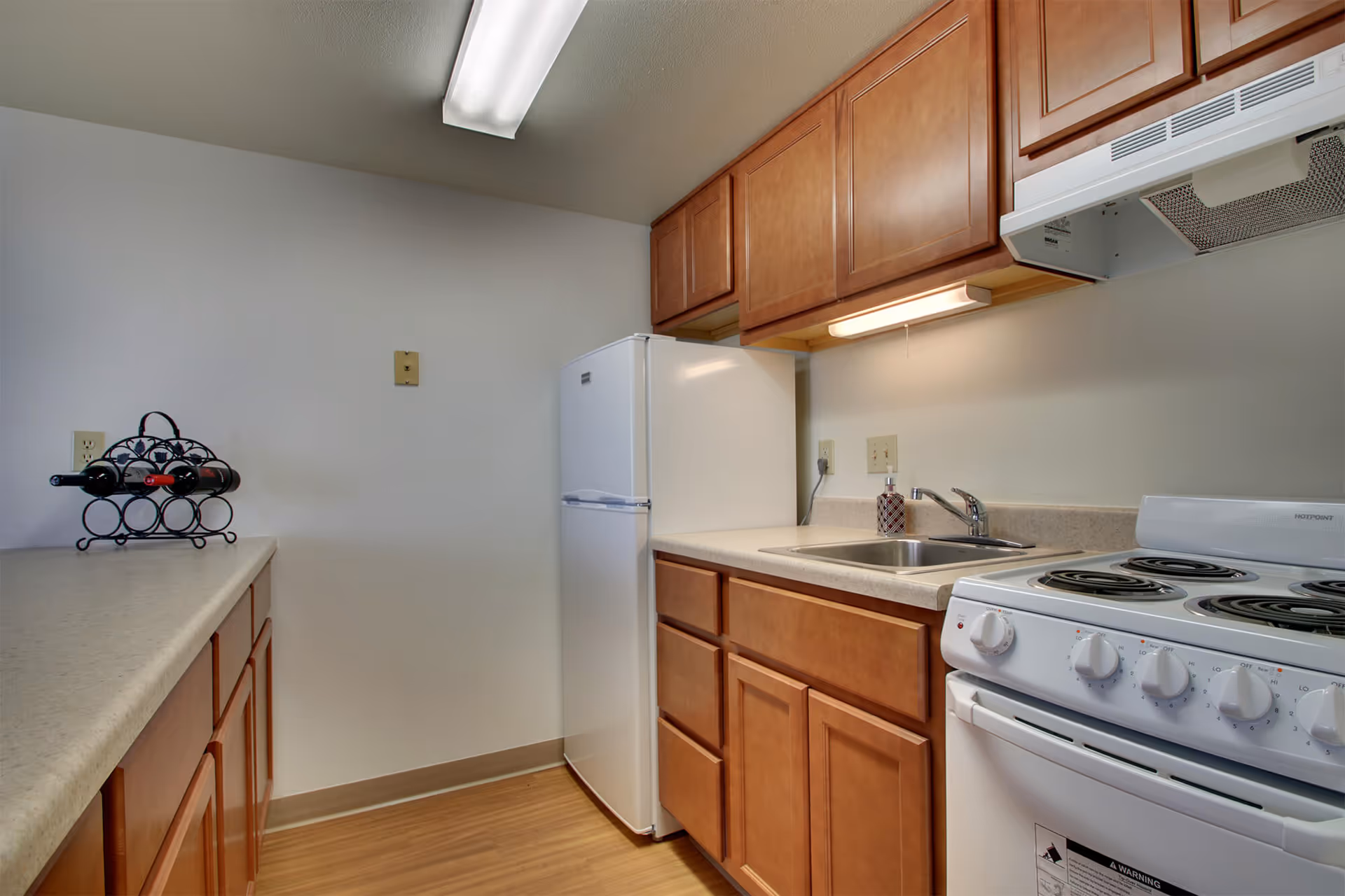 Compact kitchen with wood cabinets, a white refrigerator and electric stove, a sink and countertops.