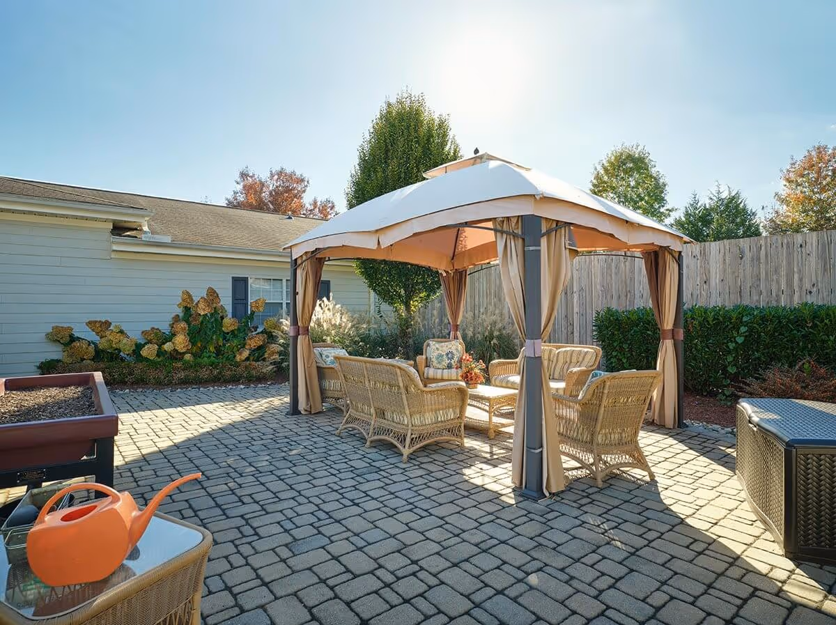 Patio with a canopy gazebo over wicker seating on a paved courtyard next to a single-story building.