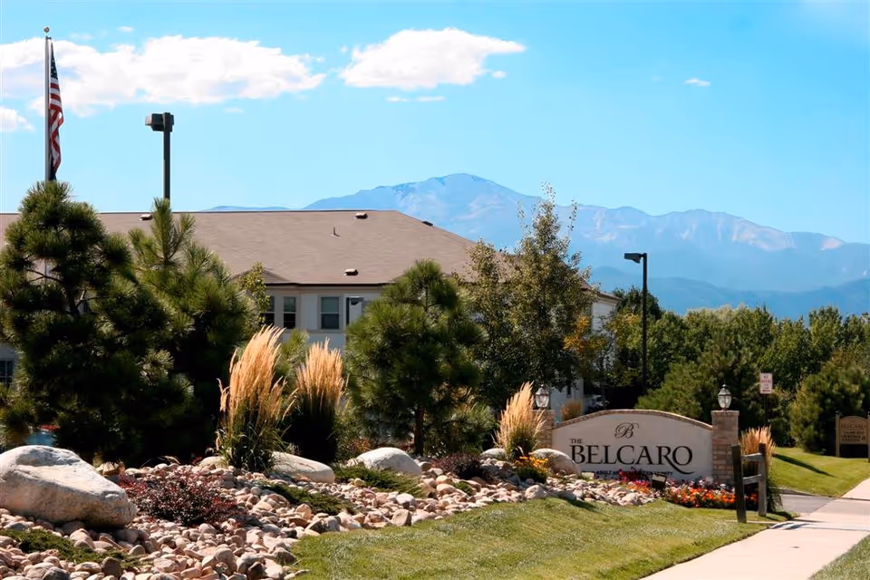 A view of The Belcaro senior living facility entrance with landscaped greenery and mountains in the background.