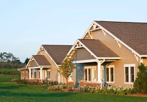 Exterior view of a row of beige senior living buildings with lawn and landscaping.