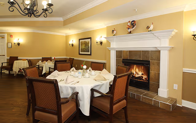 Cozy dining room with round tables set for a meal and a lit fireplace.