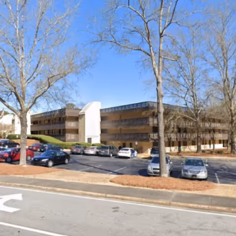 Exterior view of Larry Moore Manor, a multi-story senior living building with a parking lot and leafless trees in the foreground.