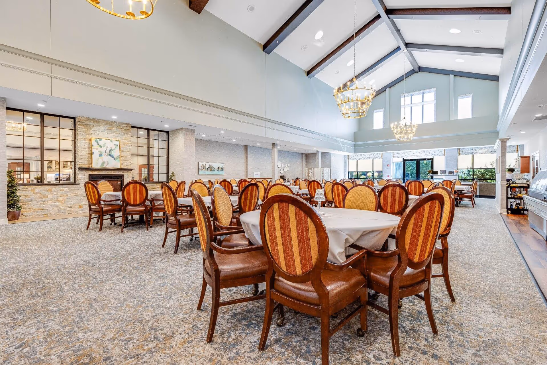 Spacious dining room with round tables and striped upholstered chairs under a vaulted ceiling with chandeliers.