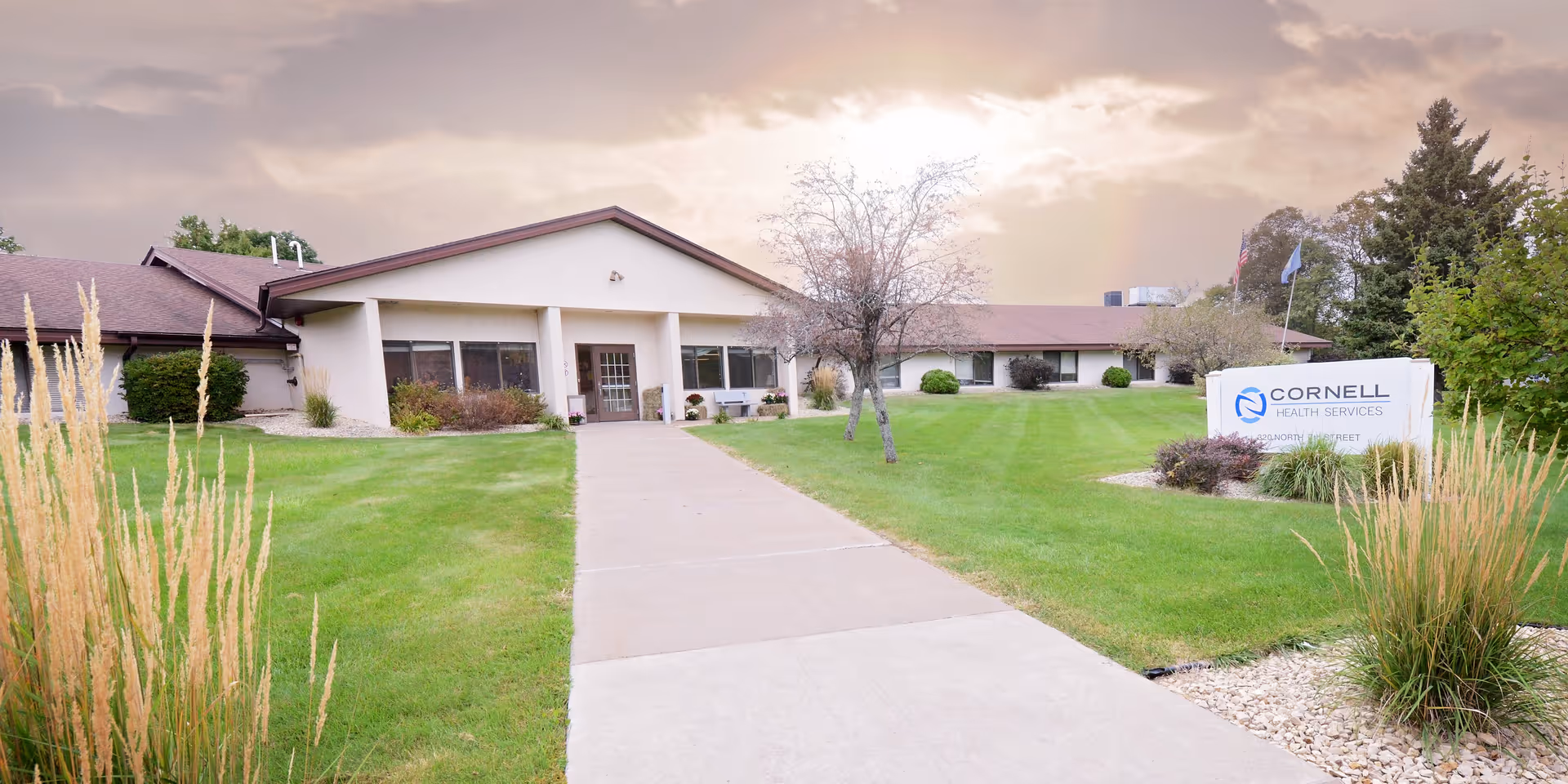 A low one-story building with a walkway leading to the main entrance and a lawn sign reading 'Cornell Health Services'.