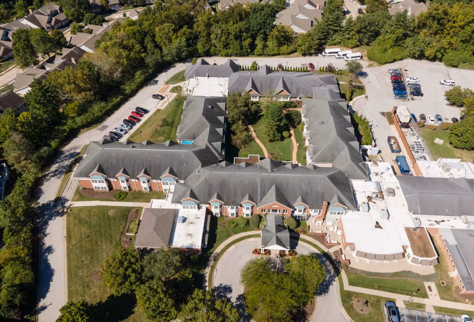 Aerial view of a U-shaped senior living facility with a central courtyard, surrounding parking lots, trees, and a circular driveway.