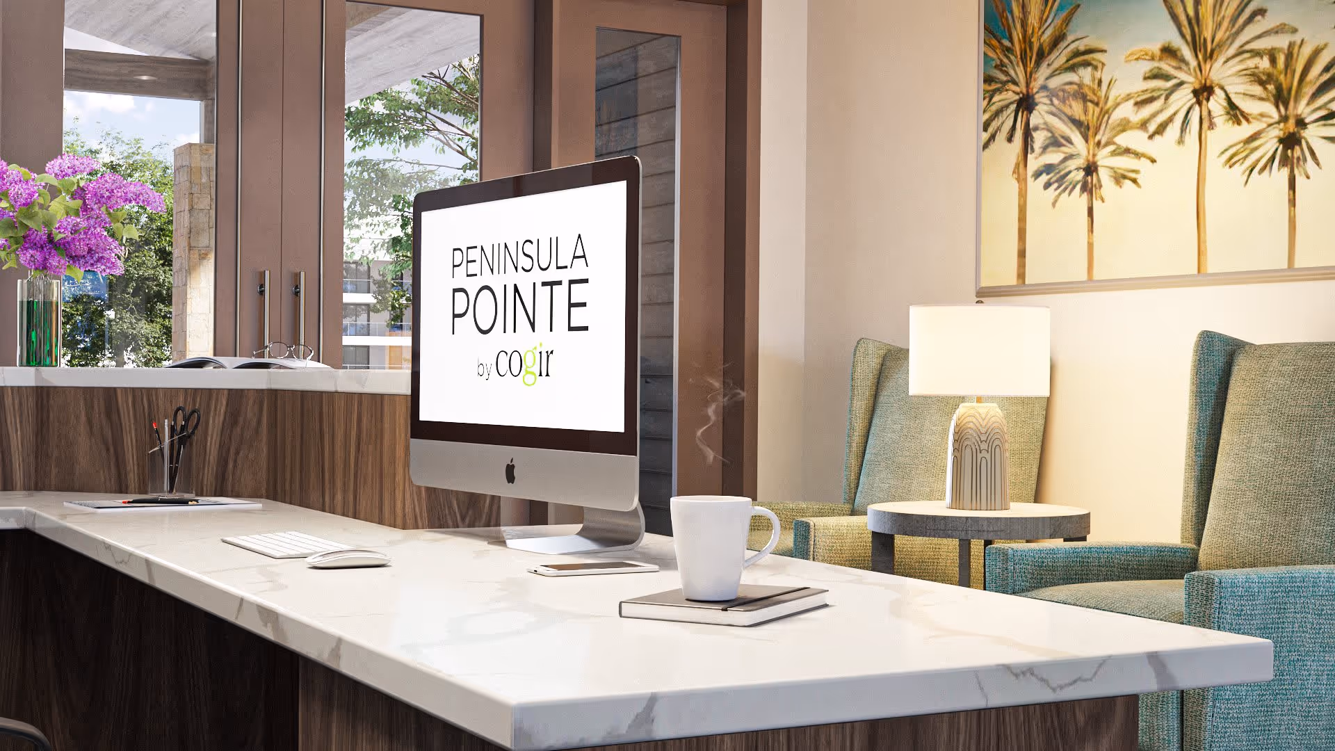 A modern reception or office area with a marble countertop desk featuring an iMac computer displaying the text 'Peninsula Pointe by Cogir'. On the desk are a steaming white coffee mug, a closed notebook, a keyboard, a mouse, and a pen holder with scissors and pens. Behind the desk are large windows showing greenery outside. To the right, there are two green upholstered armchairs with a small round table between them holding a lit table lamp. A painting of palm trees hangs on the wall above the chairs.