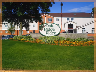 Front exterior of a multi-story senior living building with a lawn and a sign that reads "Oak Ridge Place".