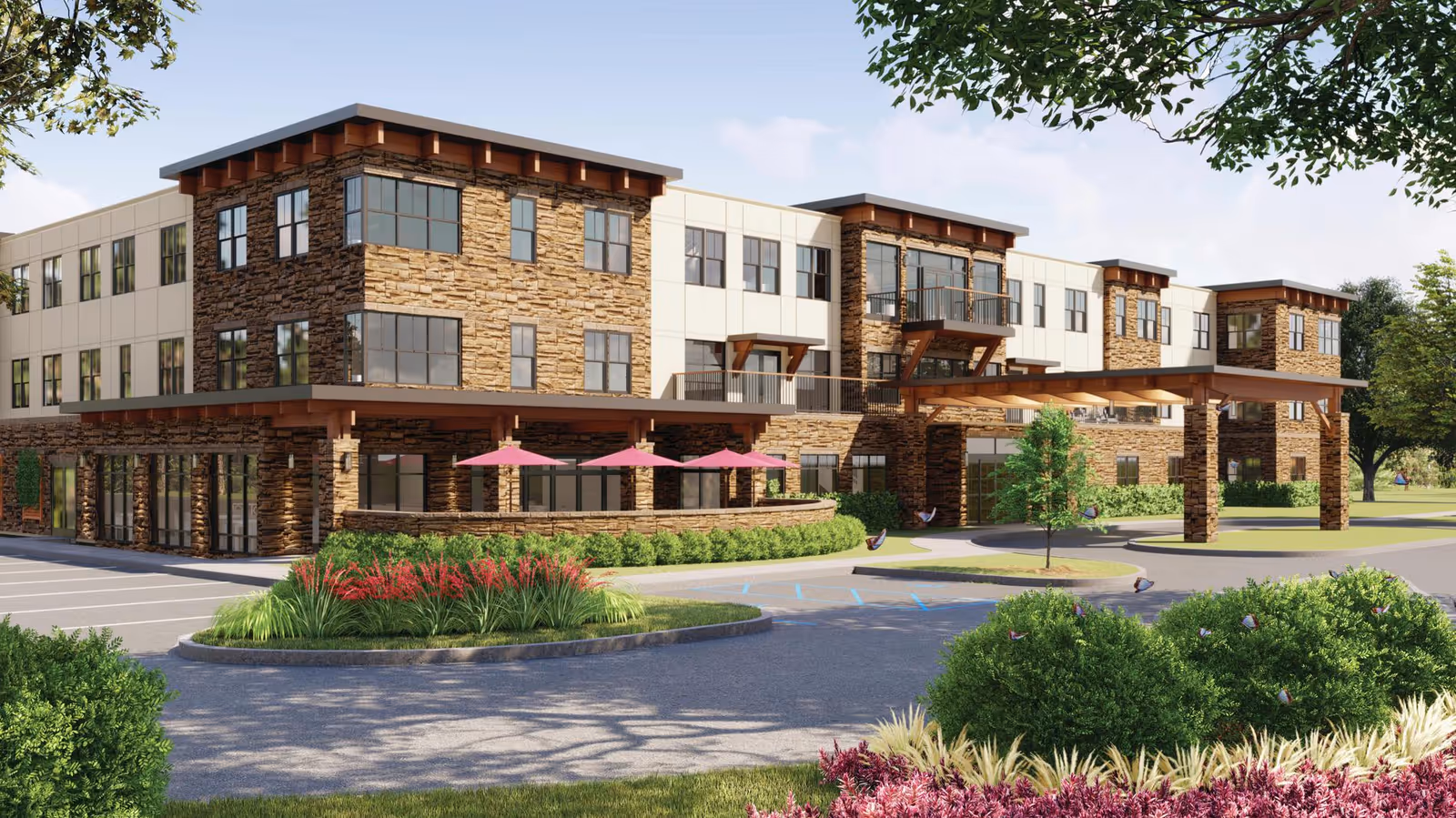 Exterior view of a modern three-story senior living facility with stone and beige paneling, large windows, a covered entrance, landscaped greenery, and outdoor seating with pink umbrellas.