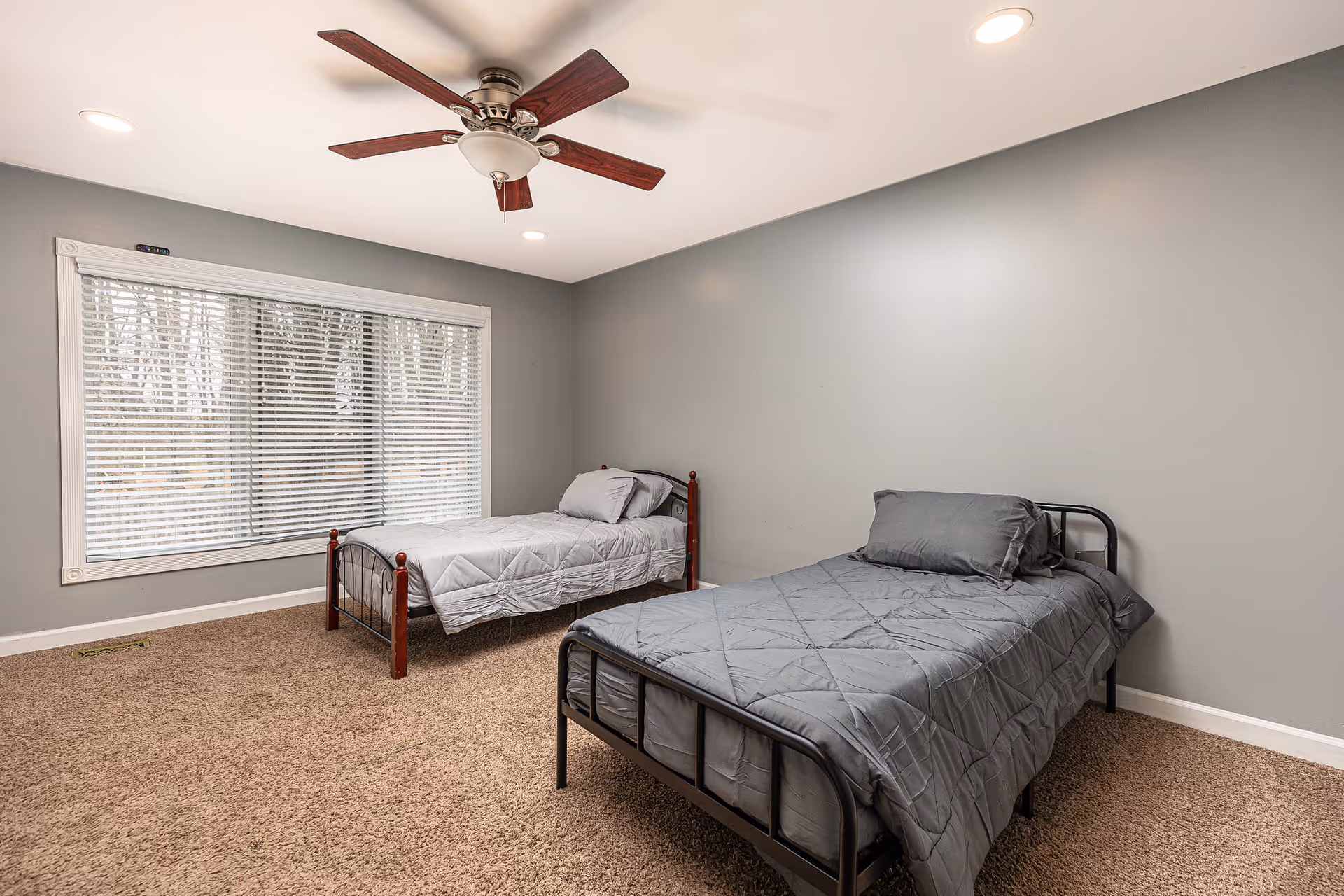 A spacious bedroom with two twin beds, gray bedding, and a ceiling fan.