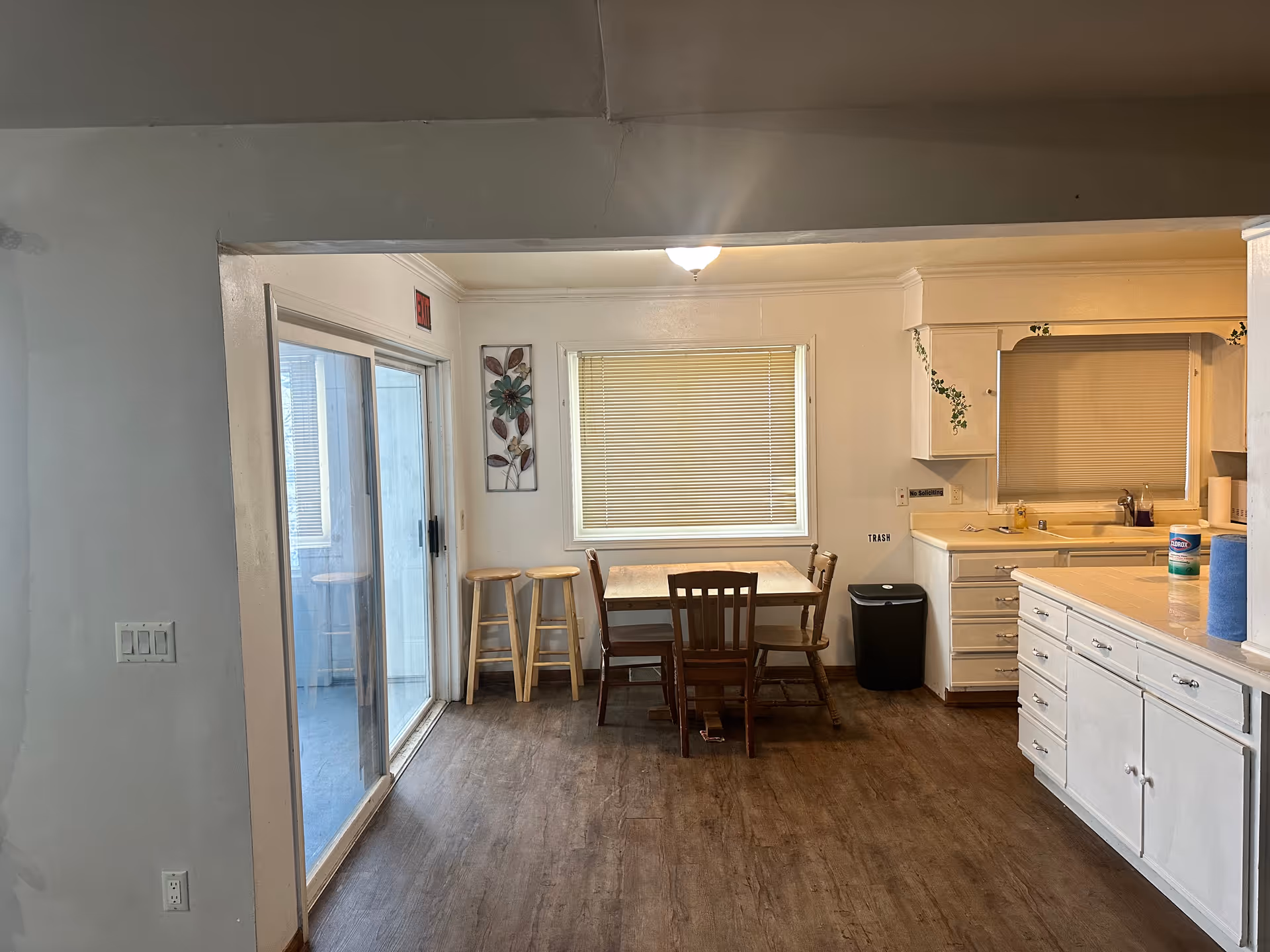 Open kitchen and dining area with a wooden table and chairs, white cabinets and countertops, a sliding glass door, and window blinds.