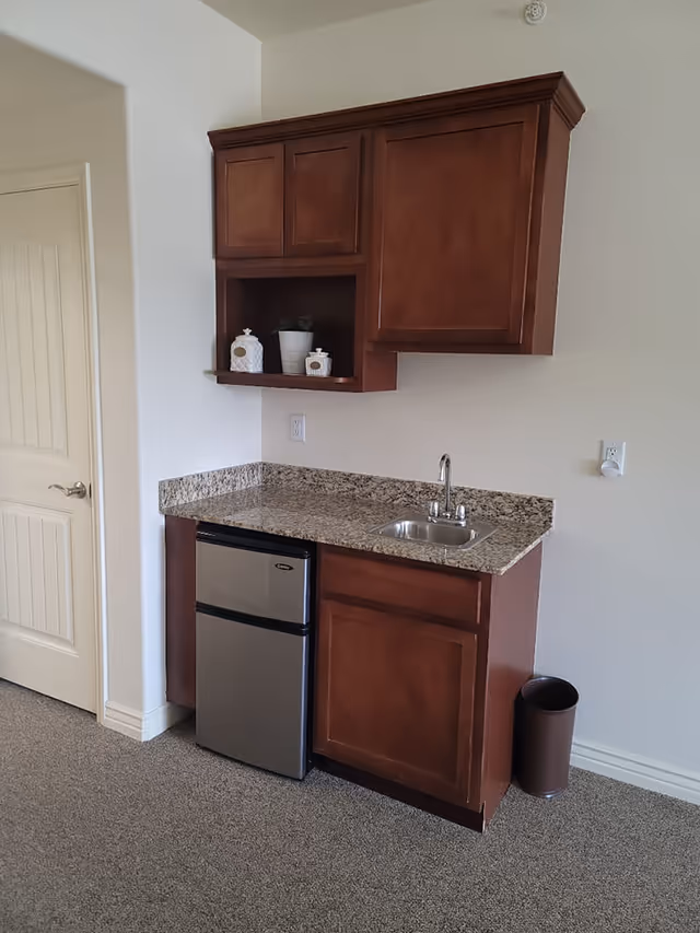 Small kitchenette with wooden cabinets, a granite countertop, mini refrigerator, and a sink.
