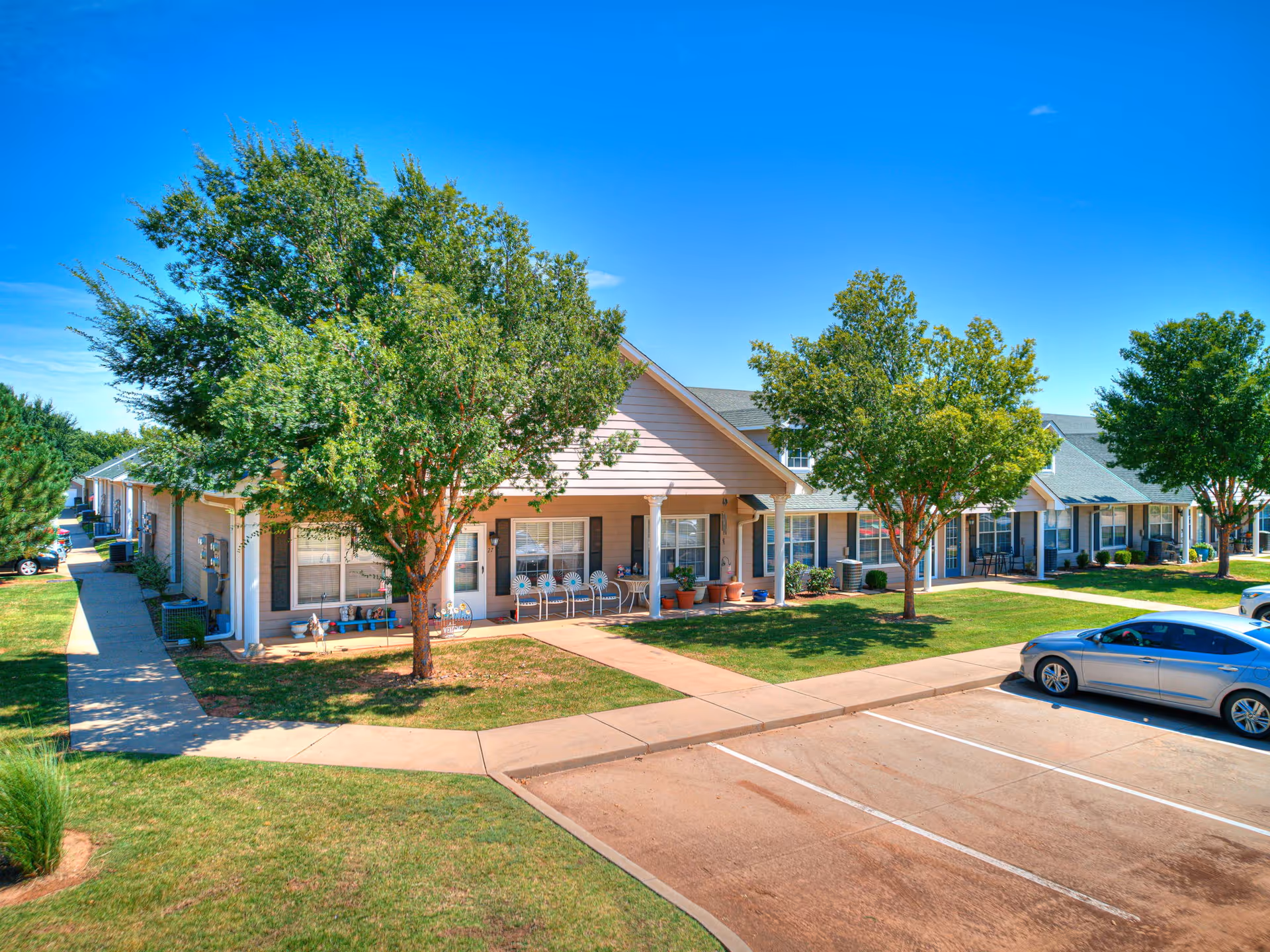 Row of single-story senior living homes with porches, trees, and a parking lot.
