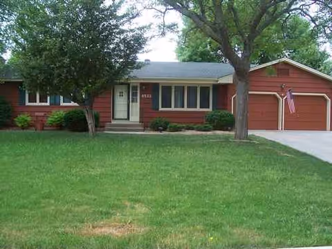 Front view of a red, single-story senior living facility with a lawn and driveway.