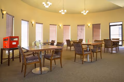 Circular dining room with tables, cushioned chairs, and warm pendant lights near windows.