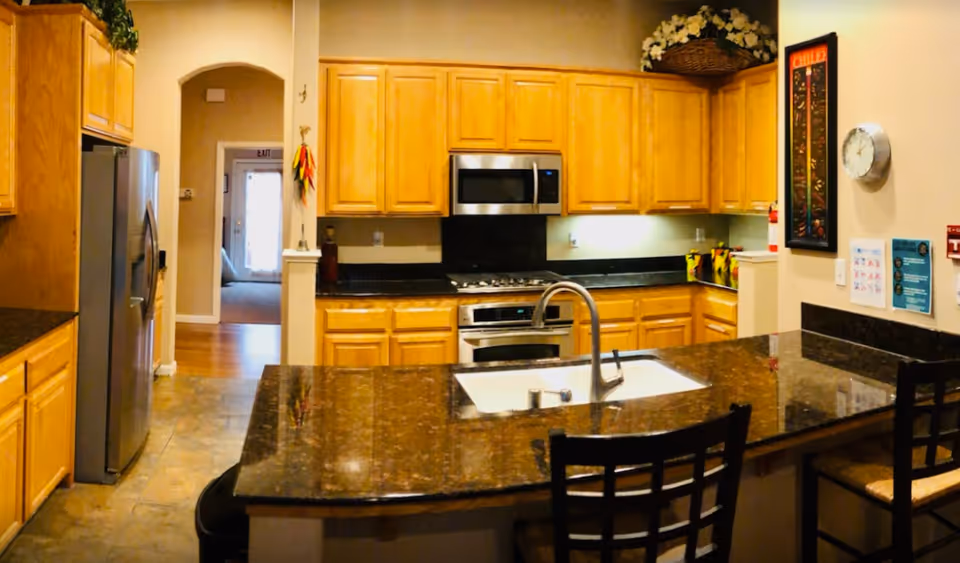 Bright kitchen with granite island, wooden cabinets, and stainless appliances.