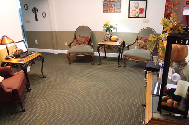 A furnished lounge with upholstered chairs, side tables, lamps and autumn decorations along a two-tone wall.